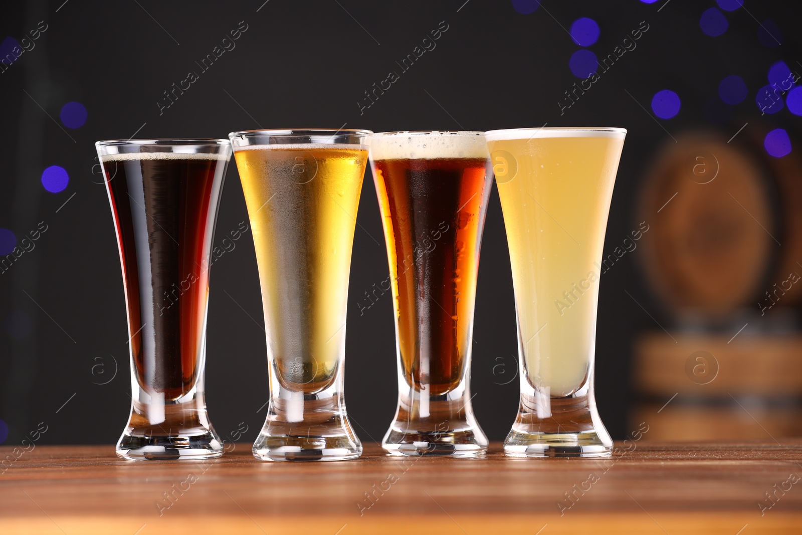 Photo of Glasses with different types of beer on wooden table against blue background, closeup