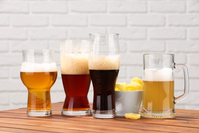 Photo of Glasses with different types of beer and snacks on wooden table against white brick wall