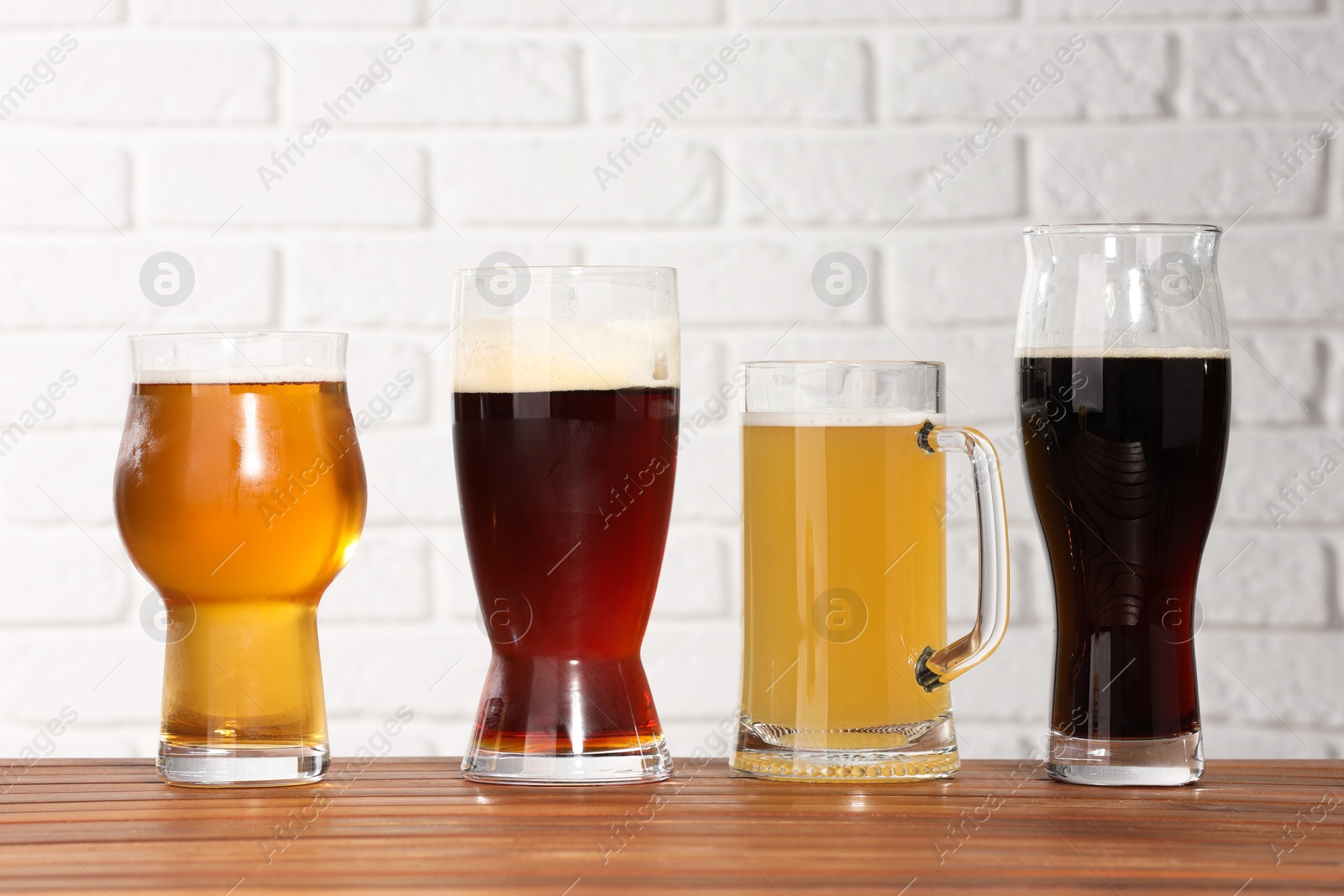 Photo of Glasses with different types of beer on wooden table against white brick wall