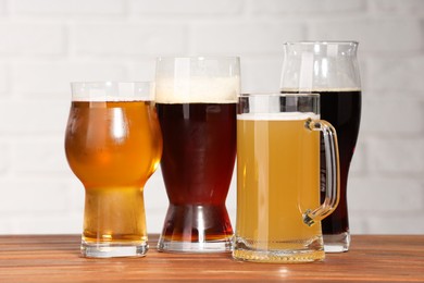 Photo of Glasses with different types of beer on wooden table against white brick wall, closeup