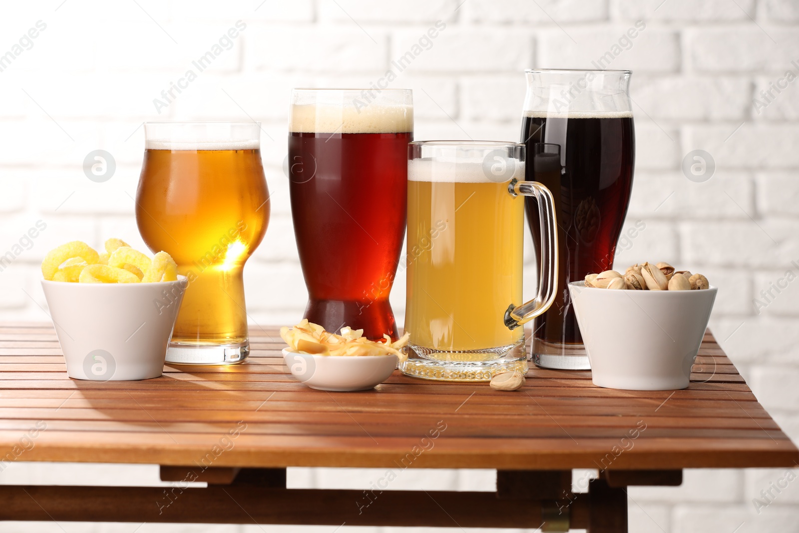 Photo of Glasses with different types of beer and snacks on wooden table against white brick wall