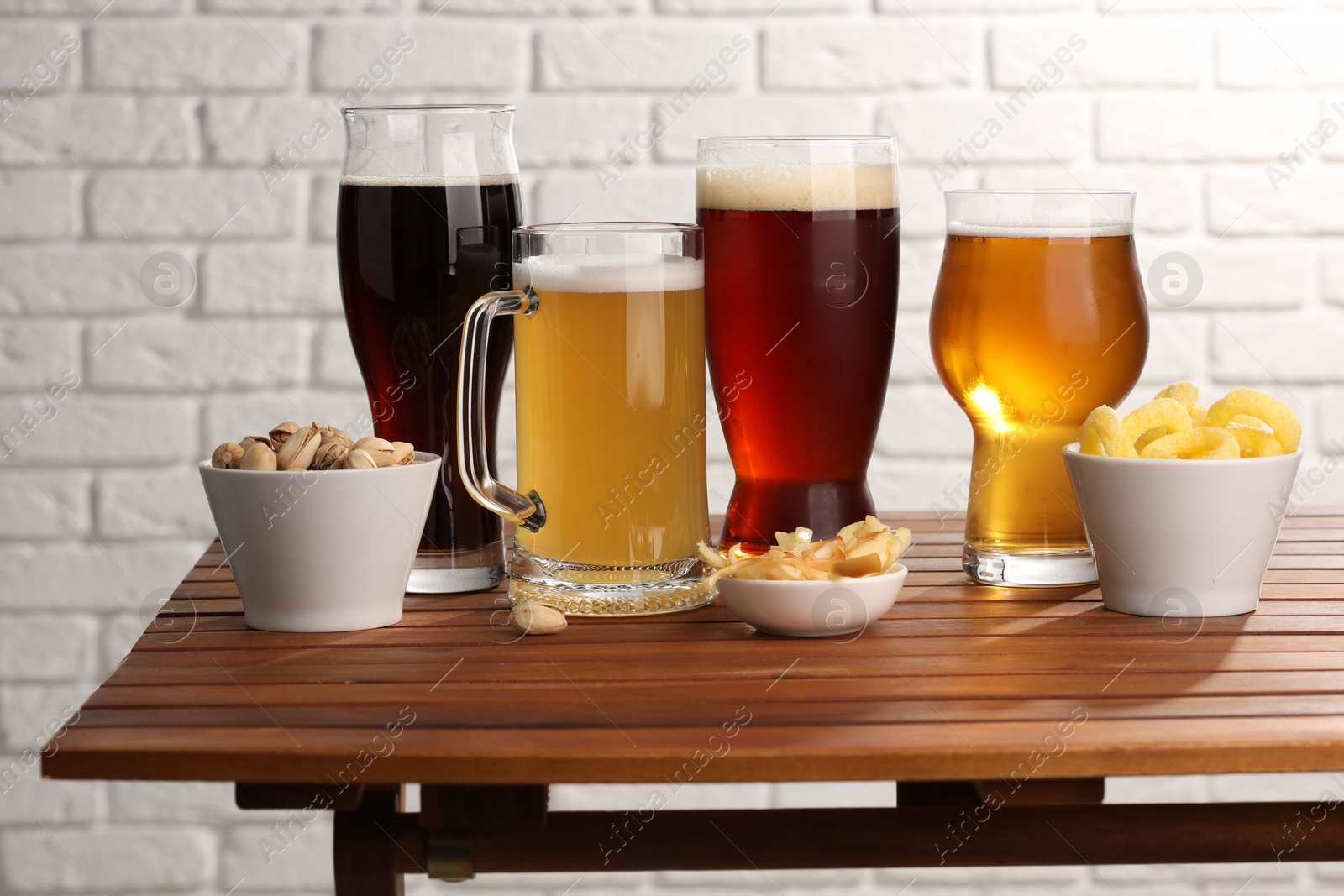 Photo of Glasses with different types of beer and snacks on wooden table against white brick wall