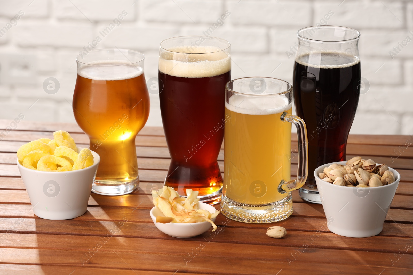 Photo of Glasses with different types of beer and snacks on wooden table against white brick wall