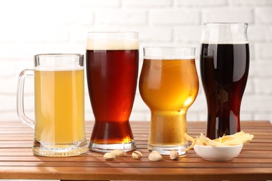 Photo of Glasses with different types of beer and snacks on wooden table against white brick wall