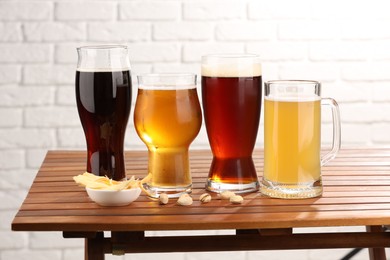 Photo of Glasses with different types of beer and snacks on wooden table against white brick wall