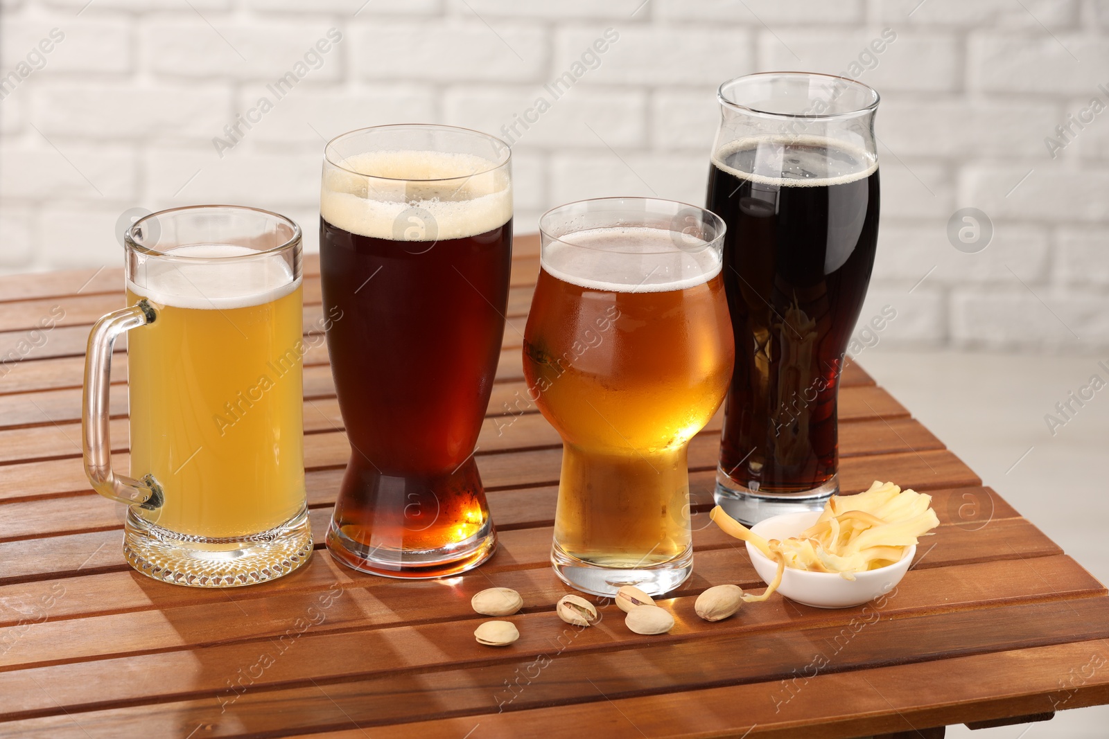 Photo of Glasses with different types of beer and snacks on wooden table against white brick wall