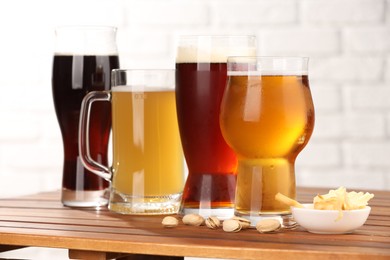 Photo of Glasses with different types of beer and snacks on wooden table against white brick wall, closeup