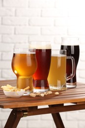 Photo of Glasses with different types of beer and snacks on wooden table