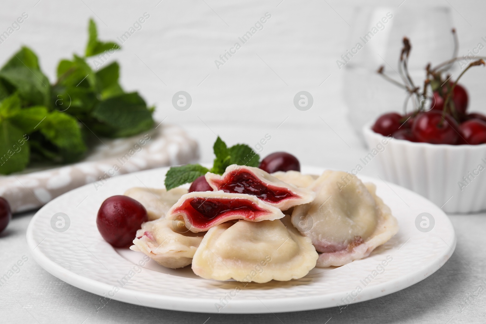 Photo of Traditional Ukrainian dumplings (varenyky) with cherries served on light table, closeup