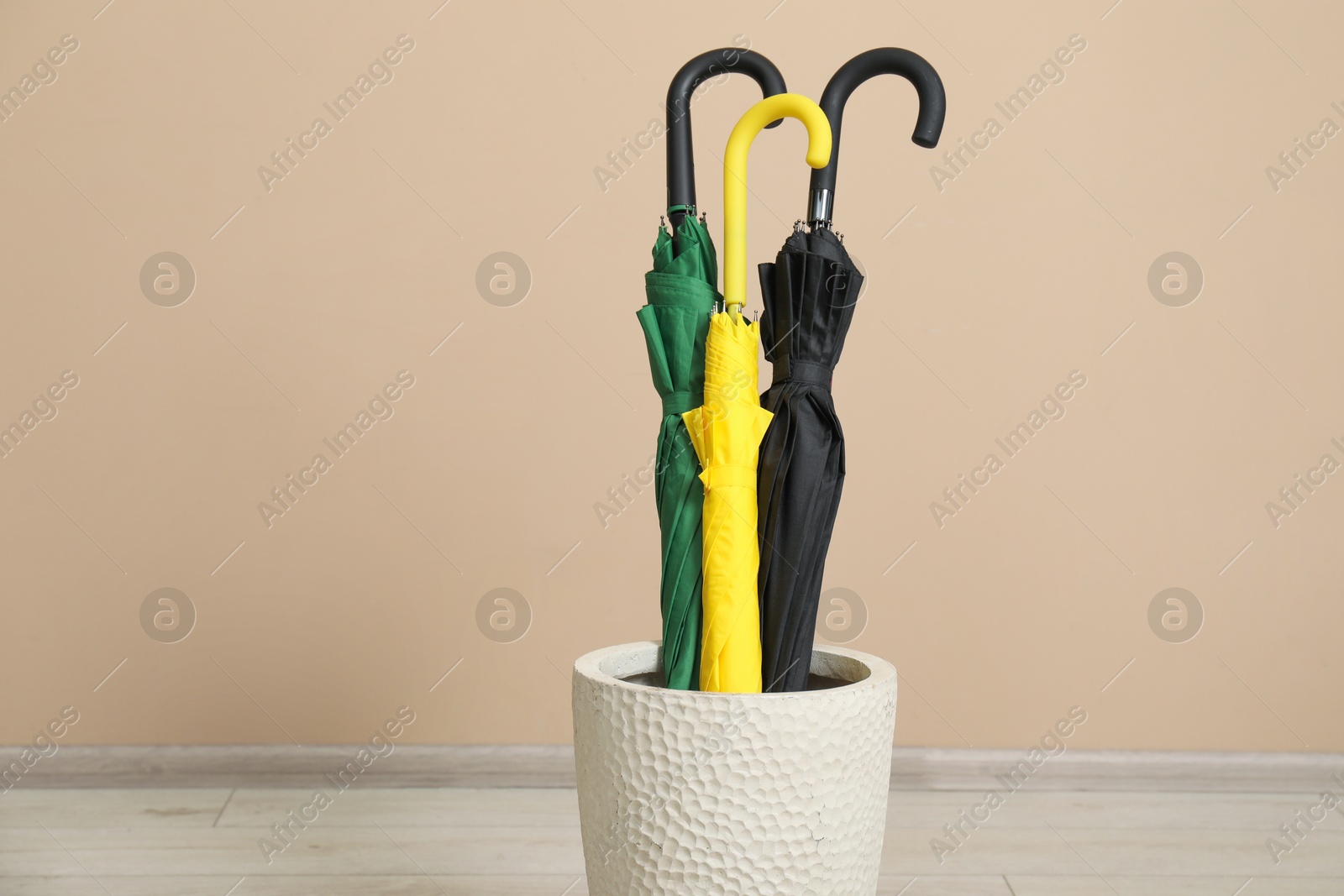 Photo of Colorful umbrellas in holder near beige wall indoors, closeup