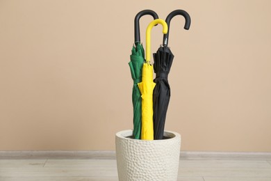 Colorful umbrellas in holder near beige wall indoors, closeup