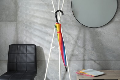 Photo of Bright umbrella on clothing rack at home