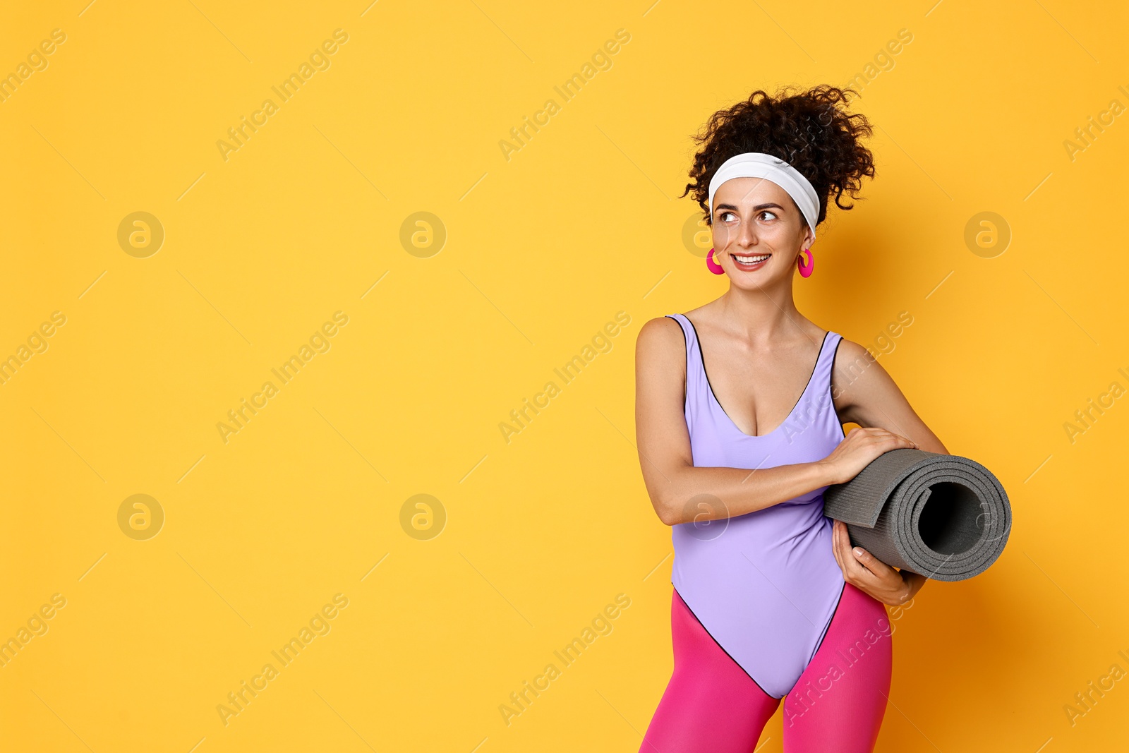 Photo of Aerobics. Woman in sportswear holding fitness mat on orange background, space for text