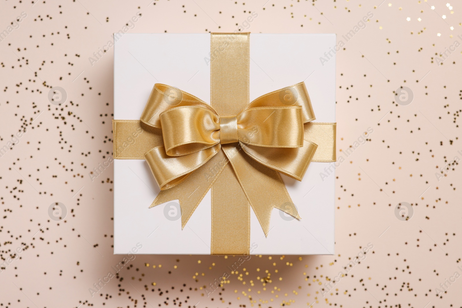 Photo of Gift box with bow and confetti on beige background, top view