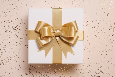 Gift box with bow and confetti on beige background, top view