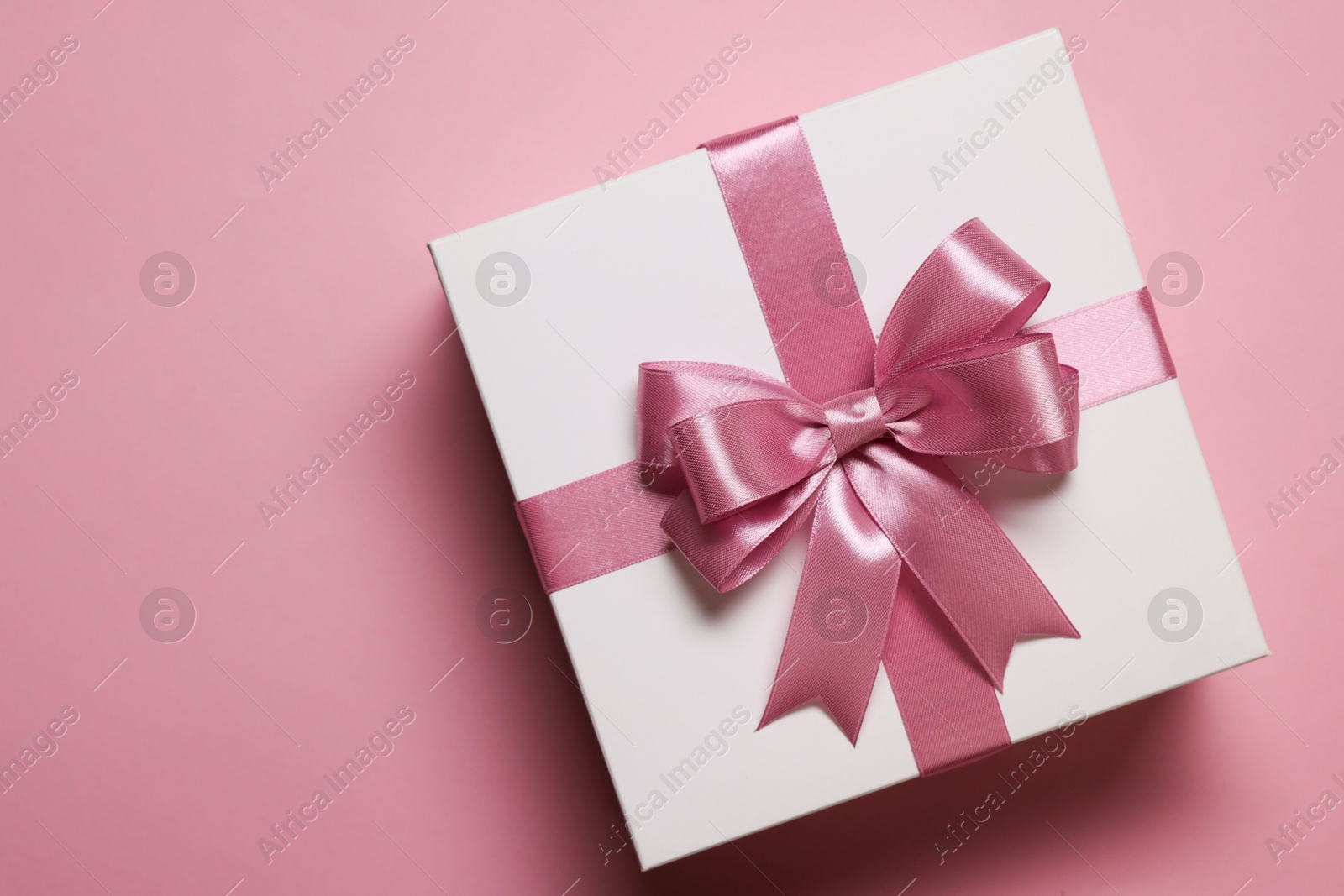 Photo of Gift box with bow on dusty pink background, top view