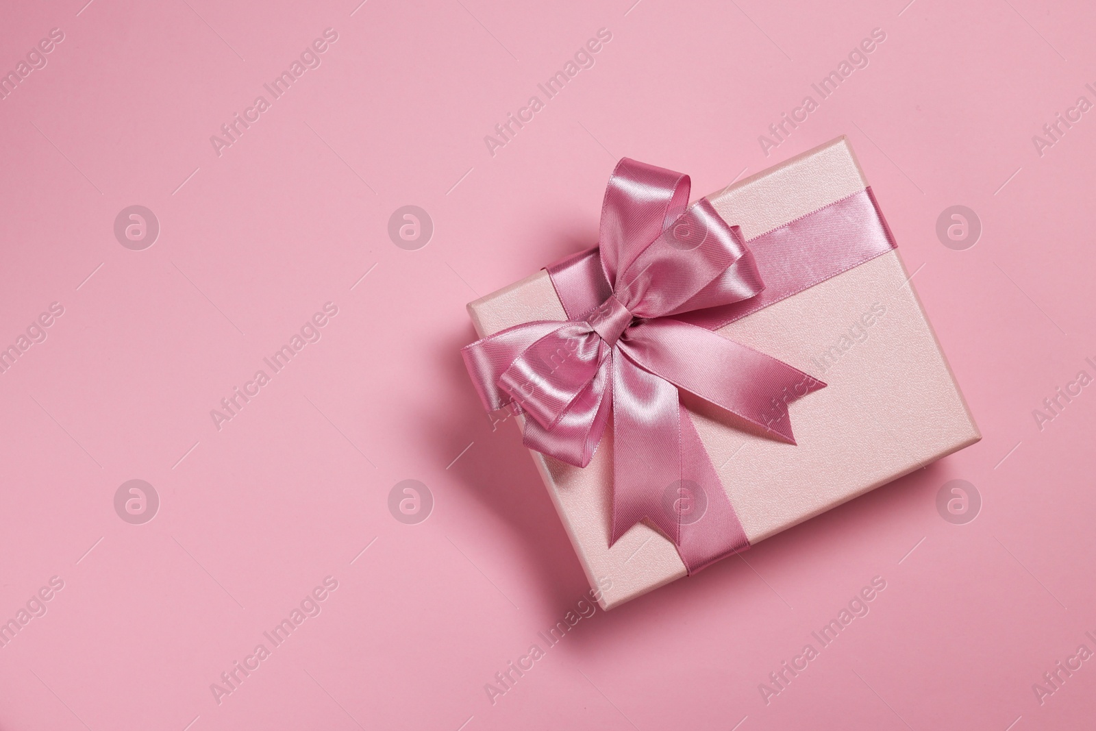 Photo of Gift box with bow on dusty pink background, top view