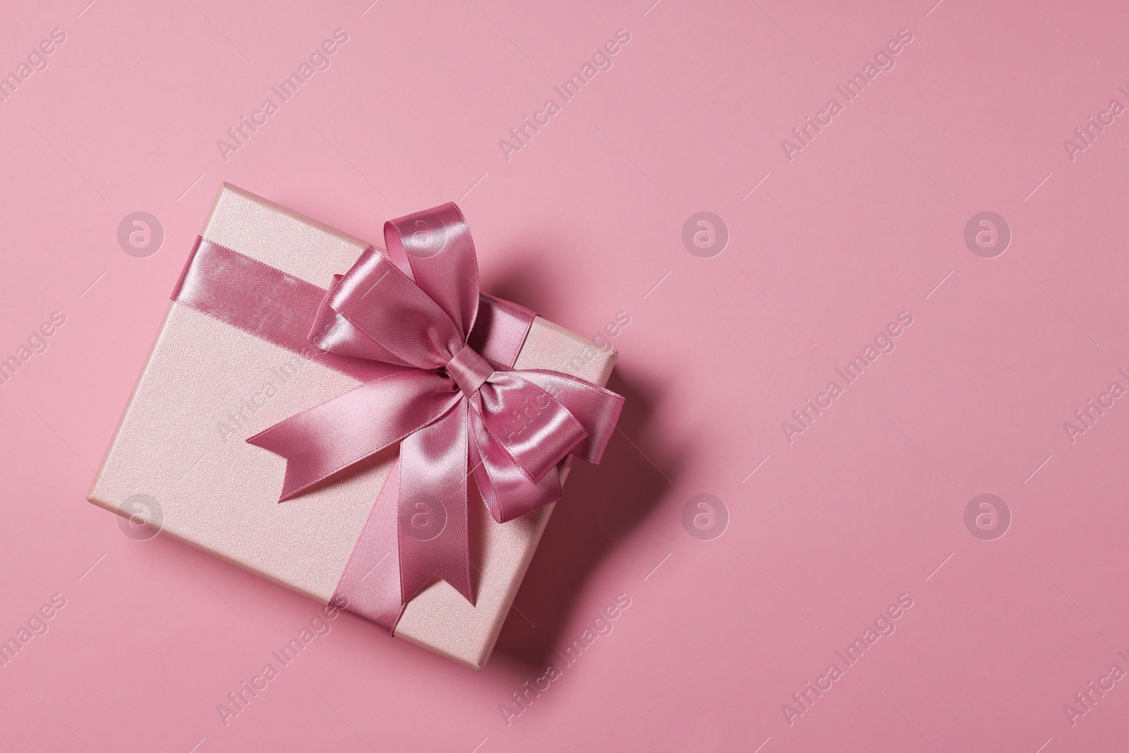 Photo of Gift box with bow on dusty pink background, top view