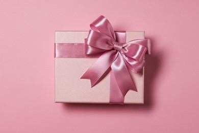 Gift box with bow on dusty pink background, top view