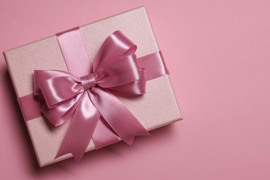 Gift box with bow on dusty pink background, top view