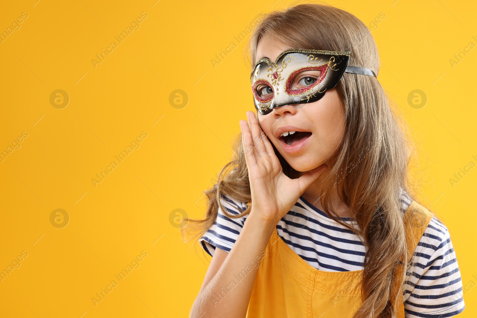 Photo of Cute girl wearing carnival mask on orange background, space for text