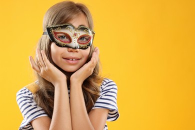 Photo of Cute girl wearing carnival mask on orange background, space for text