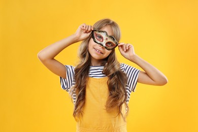 Cute girl wearing carnival mask on orange background