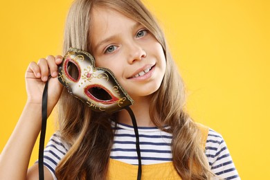 Photo of Cute girl with carnival mask on orange background