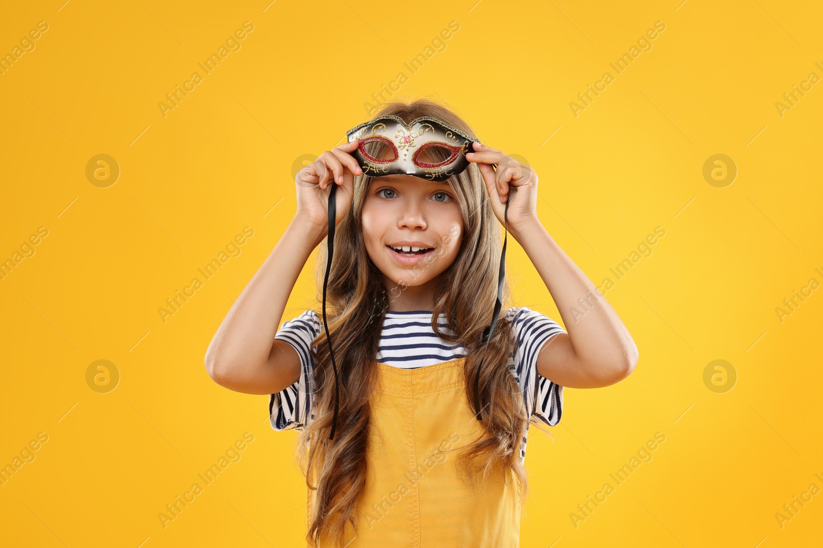 Photo of Cute girl wearing carnival mask on orange background