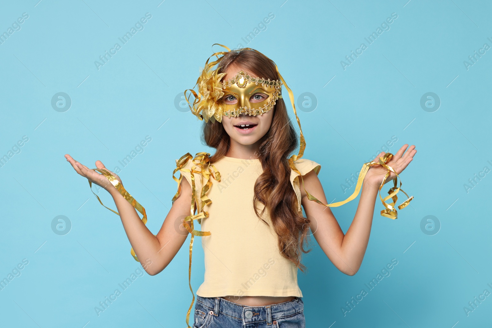 Photo of Cute girl wearing carnival mask and tinsel on light blue background