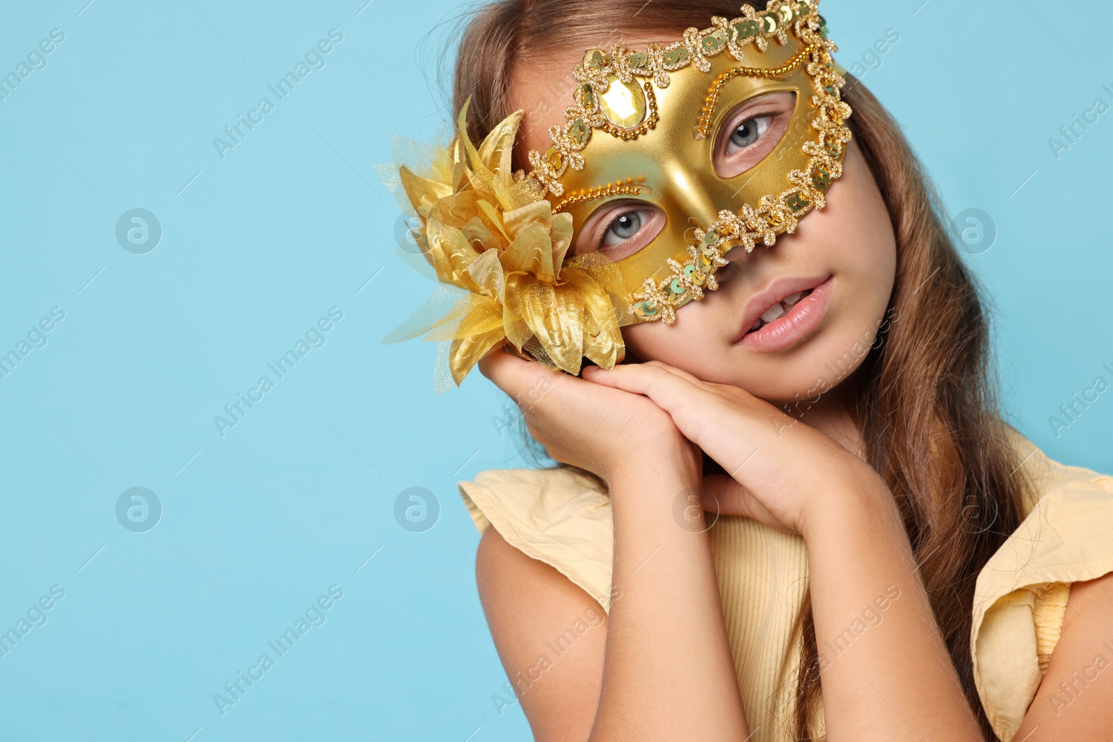 Photo of Cute girl wearing carnival mask on light blue background, space for text