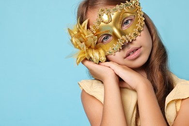 Cute girl wearing carnival mask on light blue background, space for text