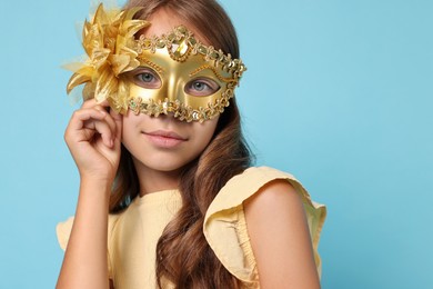 Photo of Cute girl wearing carnival mask on light blue background