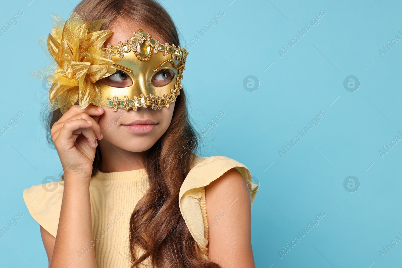 Photo of Cute girl wearing carnival mask on light blue background, space for text