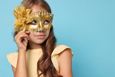 Photo of Cute girl wearing carnival mask on light blue background, space for text