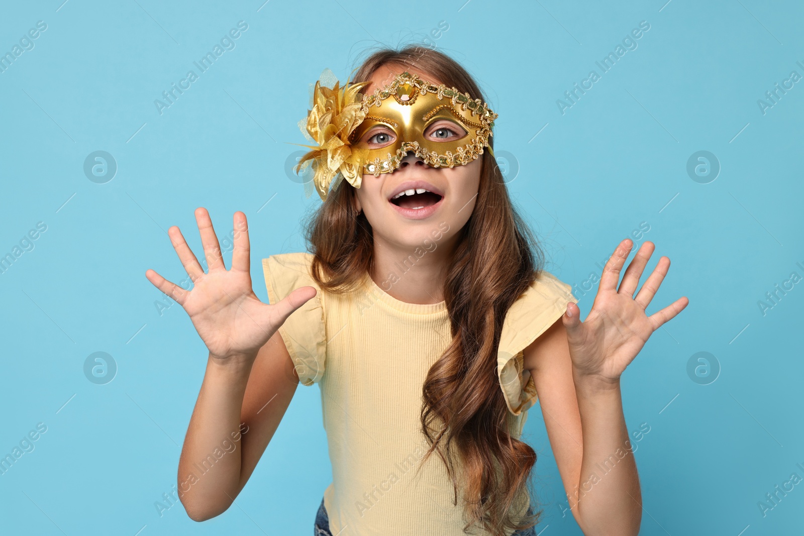 Photo of Cute girl wearing carnival mask on light blue background