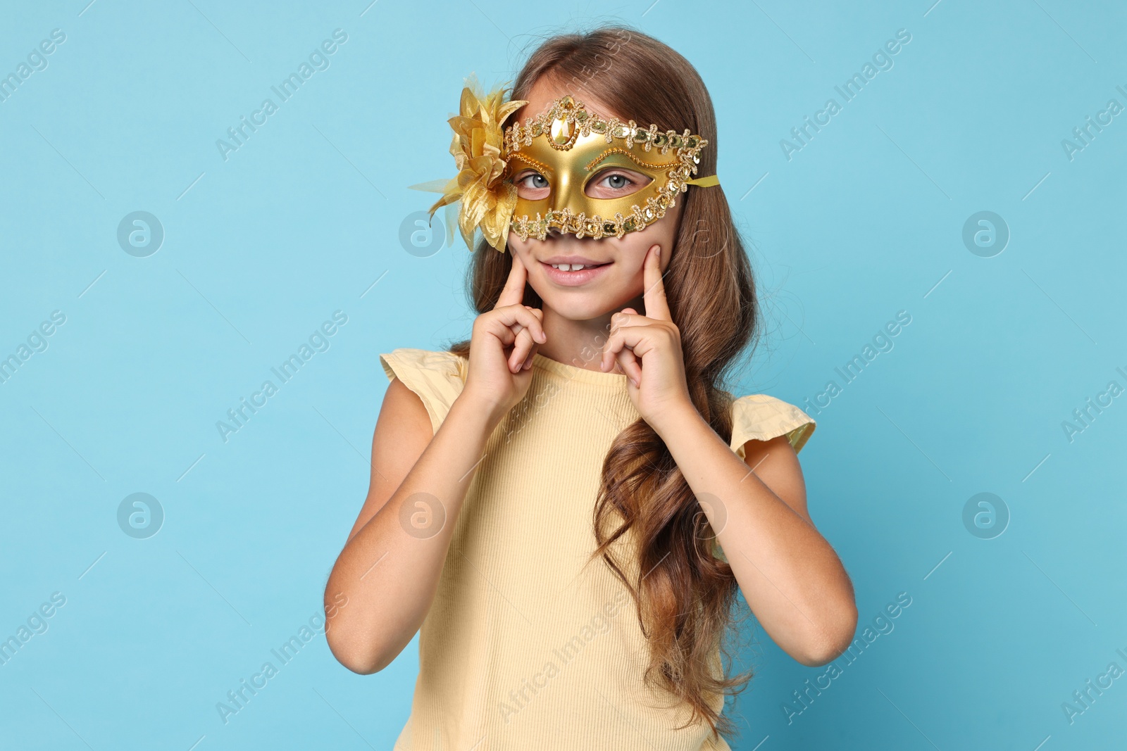 Photo of Happy girl wearing carnival mask on light blue background