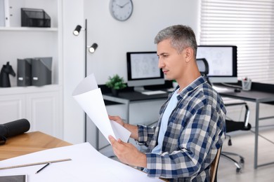 Photo of Architect with engineering drawing at wooden table in office