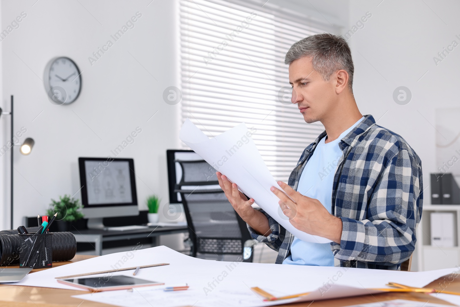 Photo of Architect checking engineering drawing at table in office