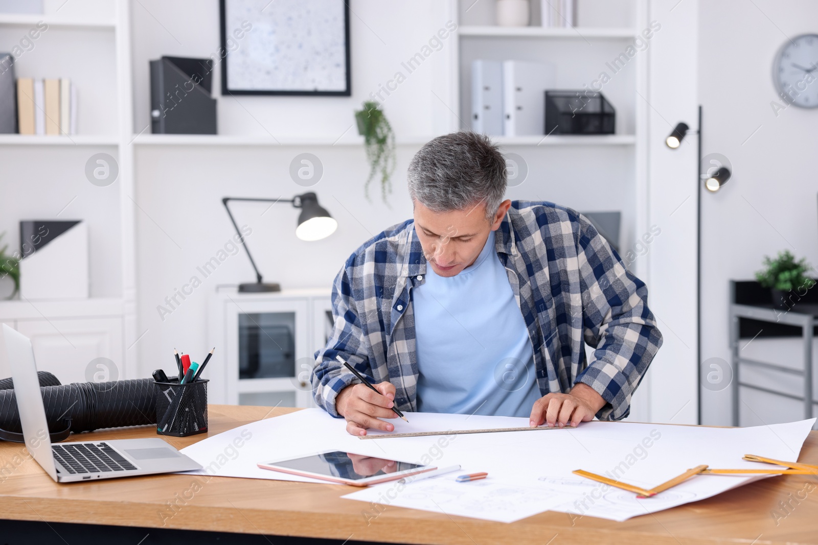 Photo of Architect making engineering drawing at wooden table in office