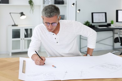 Photo of Architect making engineering drawing at wooden table in office