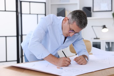 Photo of Architect making engineering drawing at wooden table in office