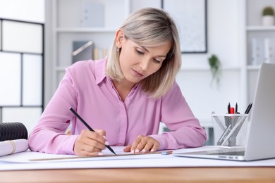 Architect making engineering drawing at wooden table in office