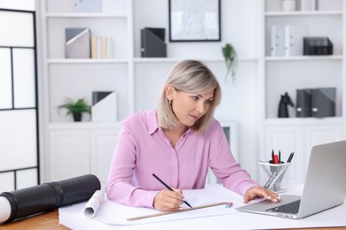 Architect making engineering drawing at table in office