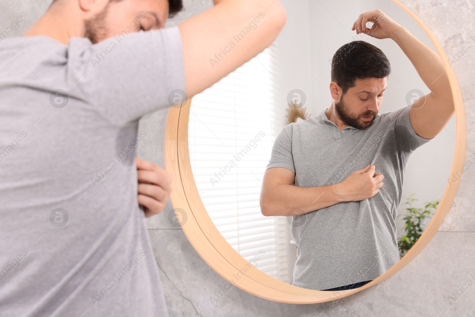 Photo of Emotional man in t-shirt before using deodorant near mirror at home