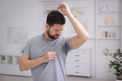 Emotional man in t-shirt before using deodorant at home