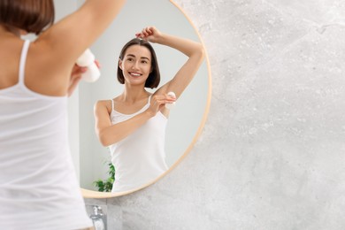 Smiling woman applying roll-on deodorant near mirror at home. Space for text