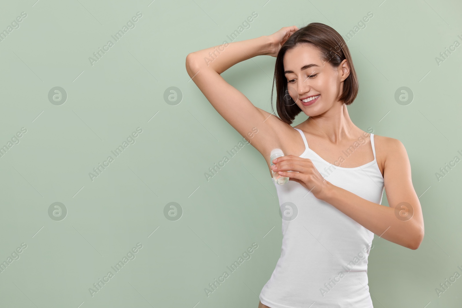 Photo of Smiling woman applying roll-on deodorant on green background. Space for text