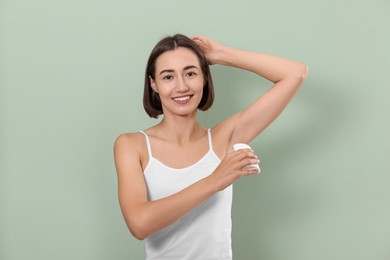 Smiling woman applying solid deodorant on green background