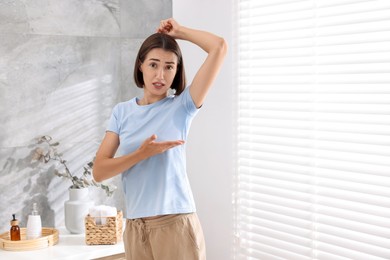 Photo of Emotional woman in t-shirt before using deodorant at home. Space for text